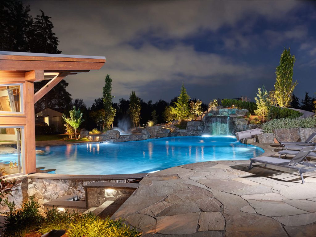 Nighttime view of a luxury pool with rock waterfall, waterslide, and illuminated landscaping.
