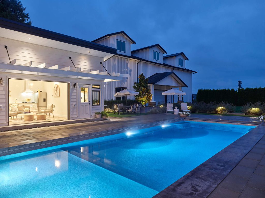 Poolhouse exterior at dusk with illuminated swimming pool and patio seating.