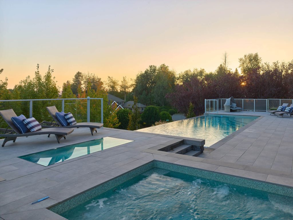 Elevated spa and infinity pool with modern paver decking and loungers at dusk.