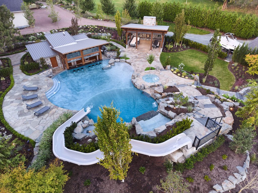 Overhead view of a custom pool with a waterslide, rock waterfall, spa, and expansive stone patio.