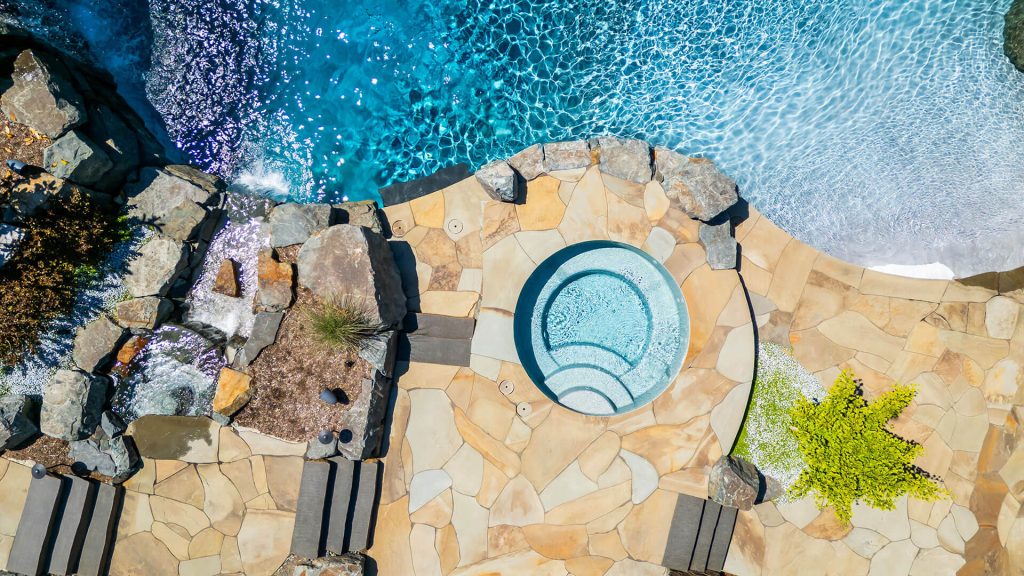 Top-down view of a custom spa, flagstone patio, and natural rock waterfall integrated into lush landscape architecture.
