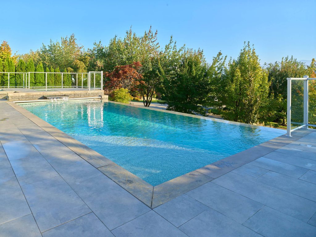 Infinity pool with large-format pavers and surrounding greenery on a modern elevated patio.