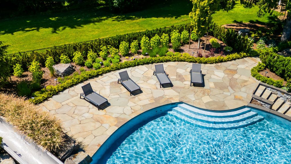 Aerial view of a luxury backyard pool with stone patio and lush landscaping, showcasing high-end outdoor living design.
