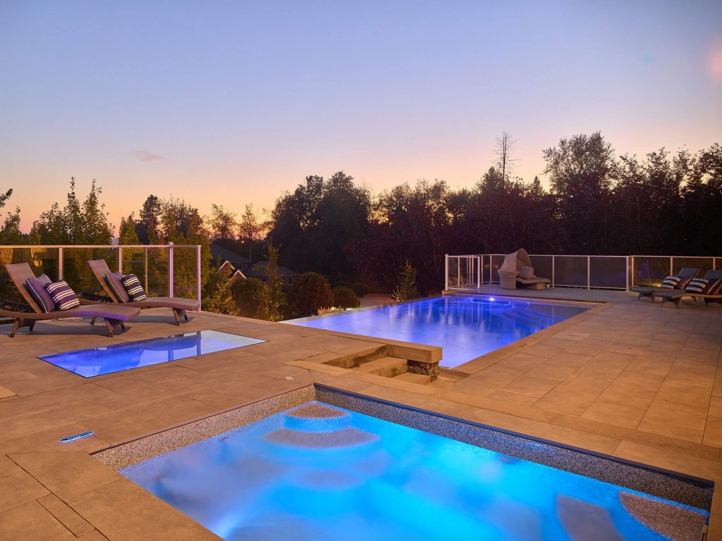 Luxury home with tiered landscape lighting, stone retaining walls, and walkway plantings at night.