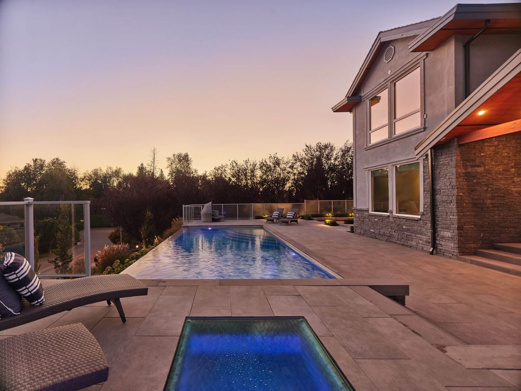 Contemporary home exterior with long modern pool and spacious patio at sunset.