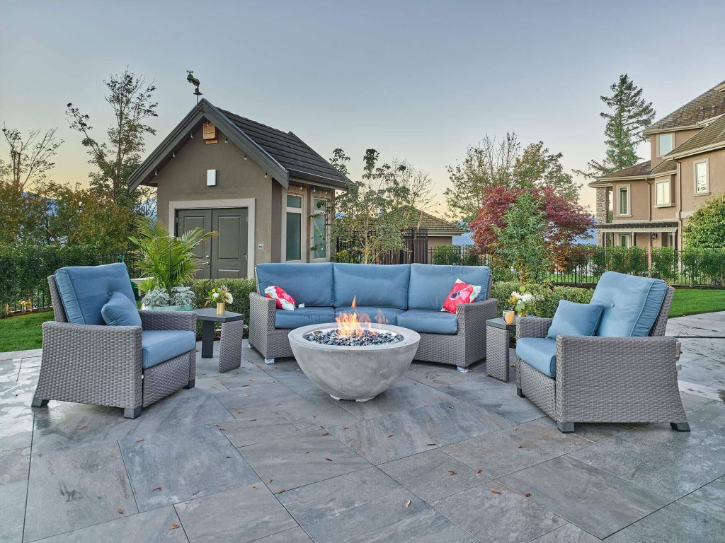 A contemporary outdoor lounge with woven patio furniture arranged around a round fire bowl centerpiece.