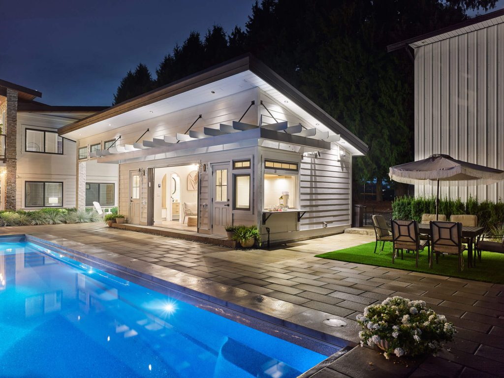 Night view of a backyard pool, poolhouse, and outdoor dining area.