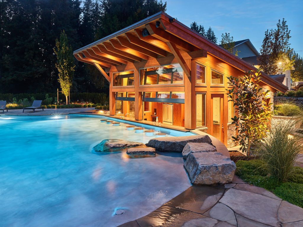 Evening scene of a swim-up bar under a timber pavilion beside a glowing custom pool.
