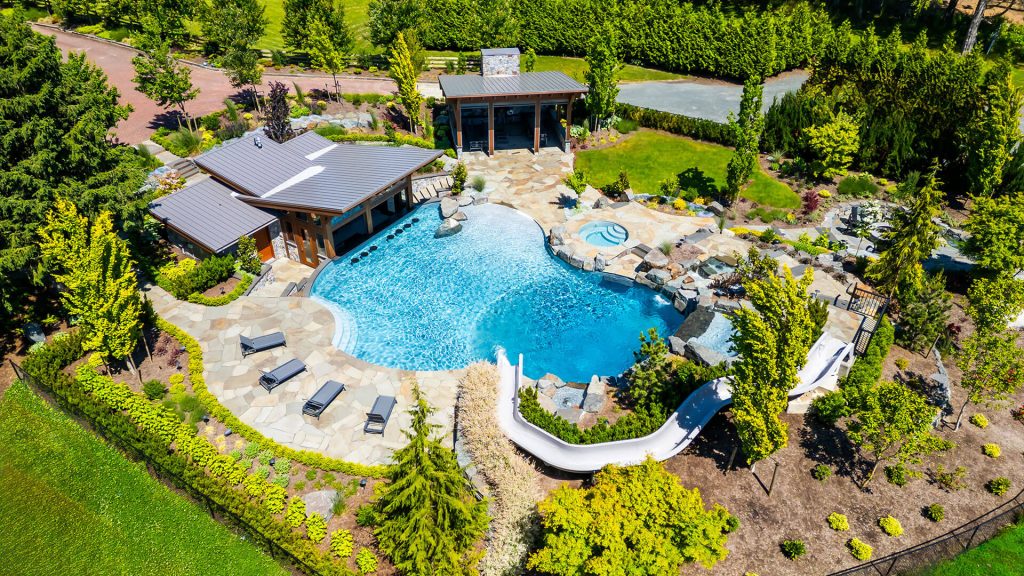 Aerial image of a resort-style pool with a long water slide, stonework, and rich plantings for a full outdoor retreat.