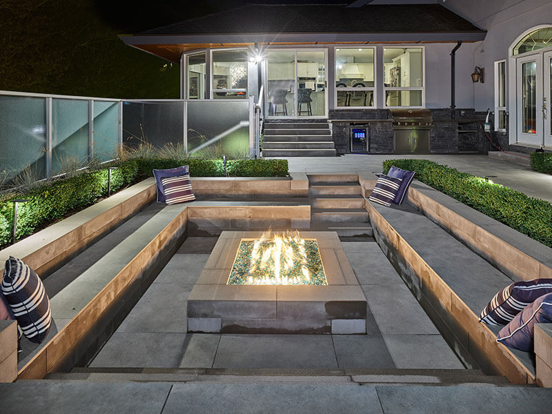 Contemporary sunken fire pit with built-in seating and architectural lighting designed by Rockwest Creative.