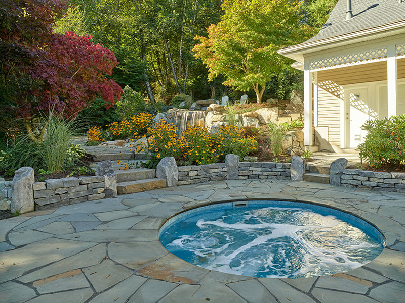 Custom stone retaining walls surrounding spa and garden areas, blending structure with natural planting design by Rockwest Creative.