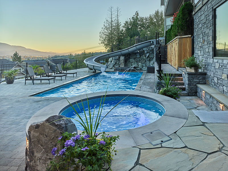 Custom pool and integrated spa with stone hardscaping and elevated waterslide by Rockwest Creative.