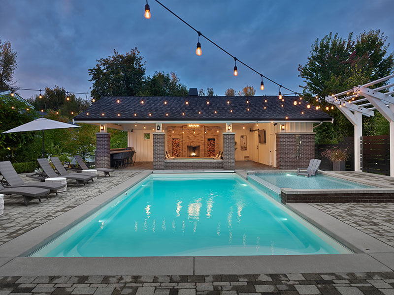 Luxury rectangular pool and spa with brick cabana, string lights, and lounge seating designed by Rockwest Creative.