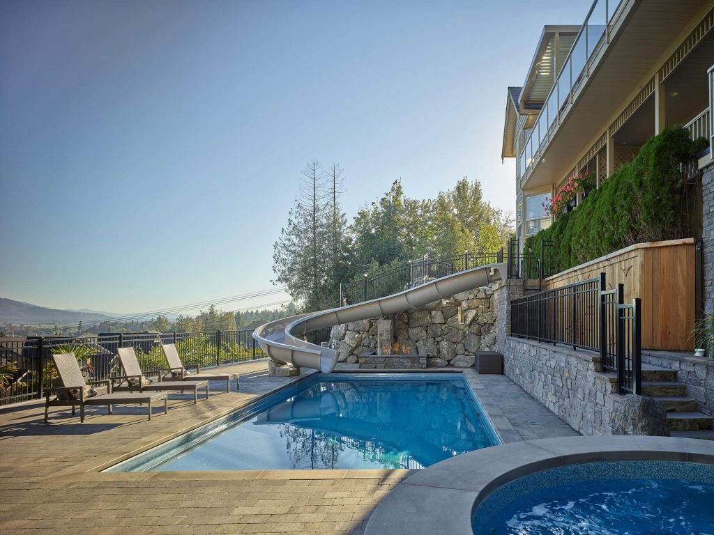 Modern pool with loungers, large waterslide, and mountain views in daylight.