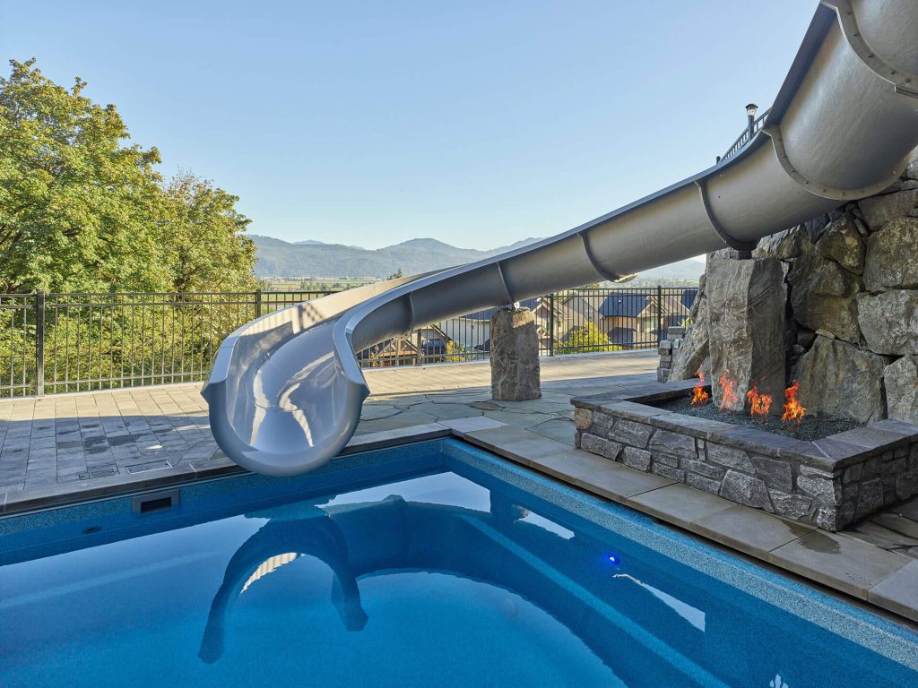 Pool waterslide leading toward a fire feature with panoramic mountain views.