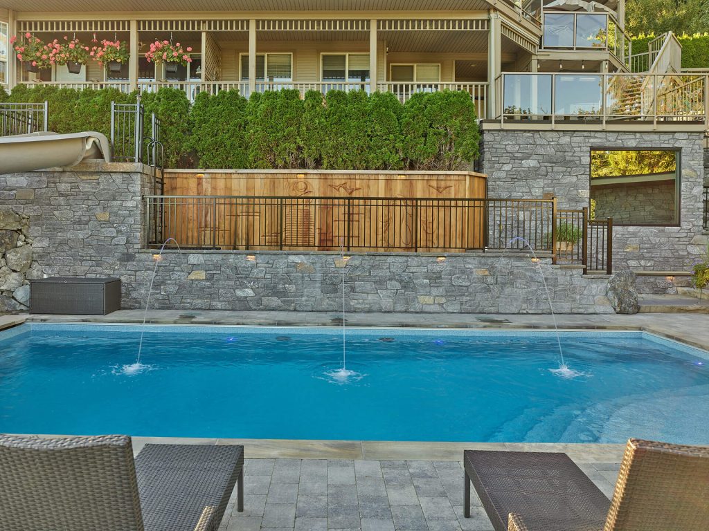Pool with deck jets and a stone retaining wall beneath an elevated patio.