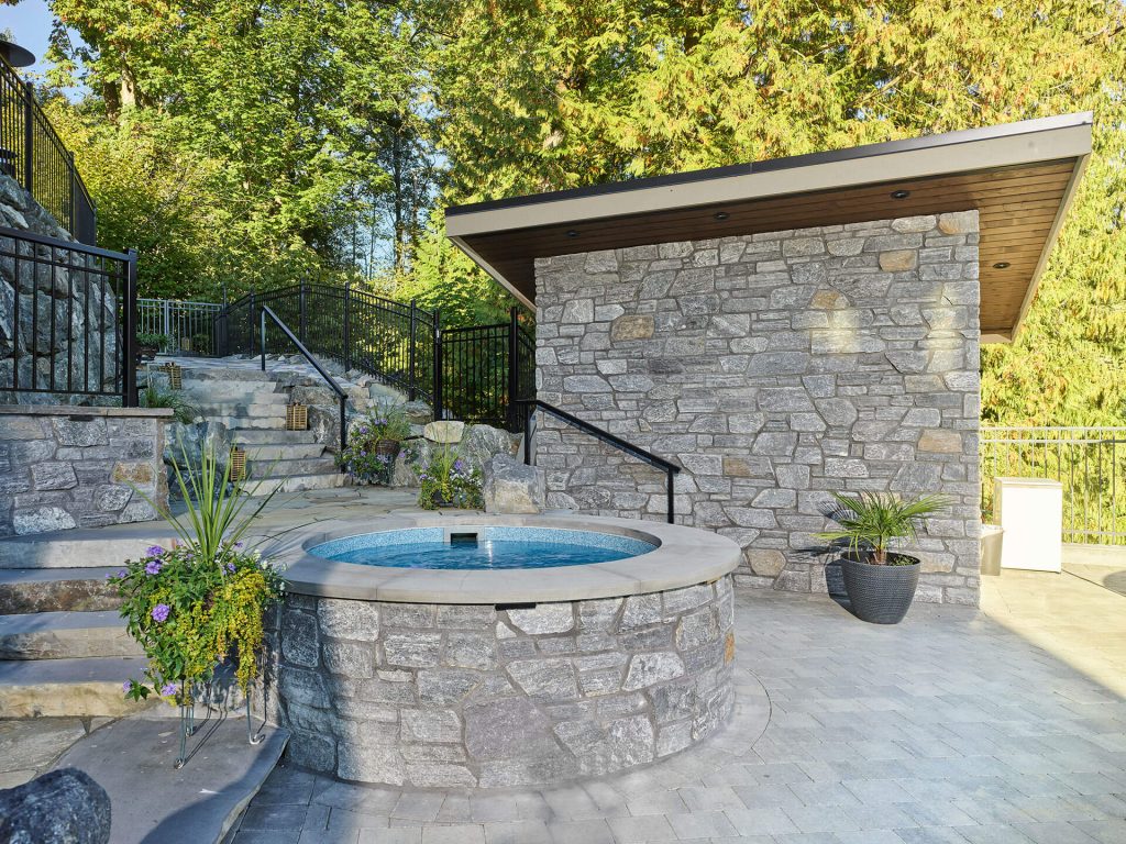 Stone-clad spa surrounded by terraced steps, natural rock, and garden landscaping.
