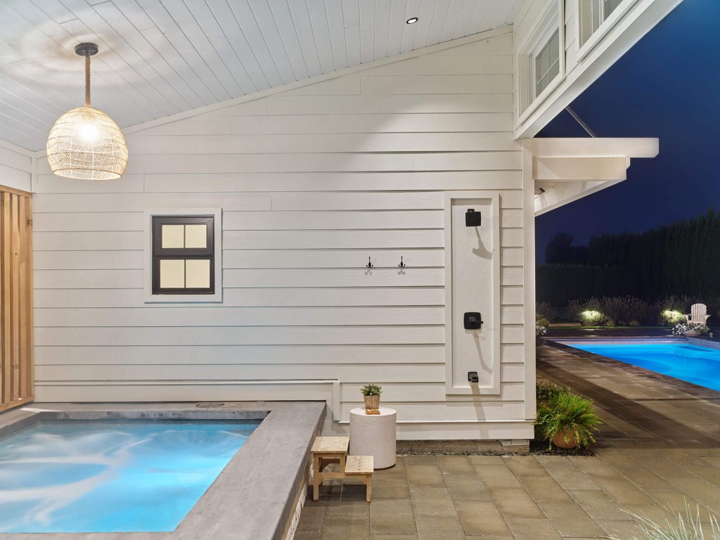 Outdoor shower and hot tub area with a view toward the illuminated pool.