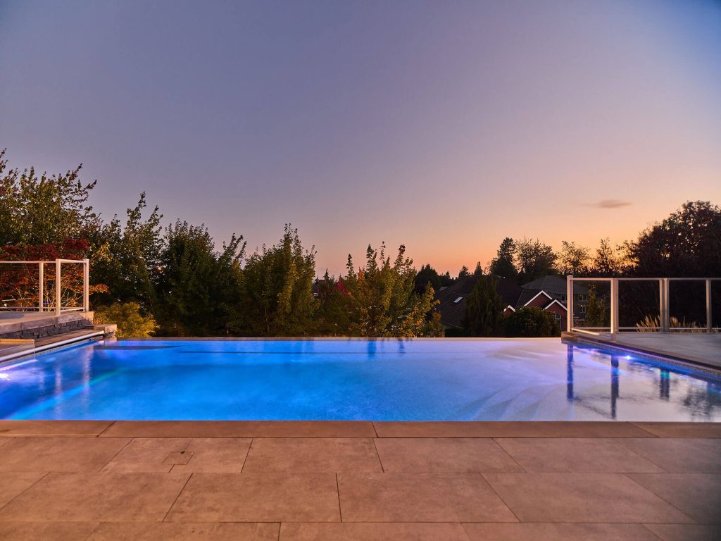 Infinity-edge pool with integrated spa overhang and lounge seating at dusk.