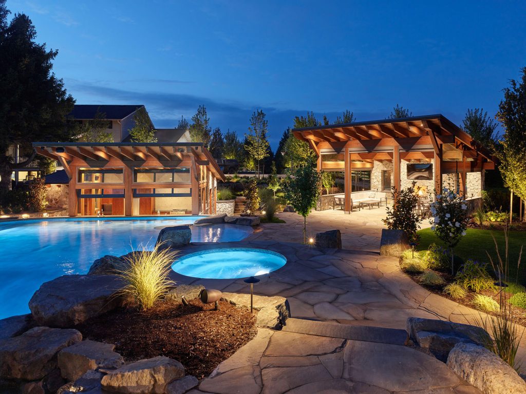 Modern pavilion and glowing spa area surrounded by stone pathways and landscape lighting at dusk.