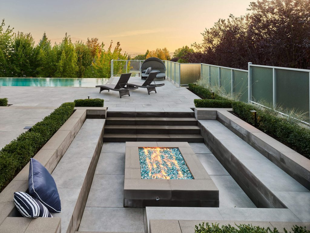 Sunken fire pit seating area overlooking an infinity pool with loungers at sunset.